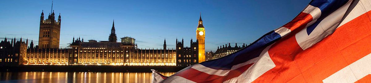 El Parlamento de Londres iluminado de noche junto a una bandera del Reino Unido